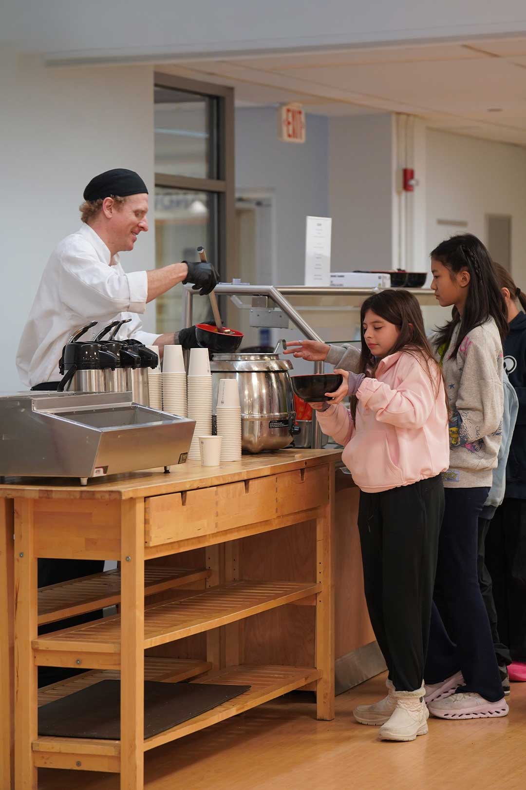 Cook serving soup in bowls to students standing in line